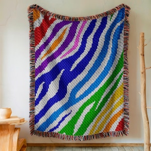Op de afbeelding: Een kleurrijk geweven deken met een regenboogzebraprint. Het deken heeft een franje rand en is gemaakt van zacht, comfortabel materiaal.