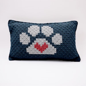 May include: A blue crocheted pillow with a white paw print design and a red heart in the center.