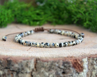 May include: A bracelet made of small, round, white and black speckled beads with a brown cord closure.