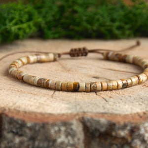 May include: A brown leather cord bracelet with small, light brown and beige stone beads.