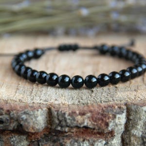Puede incluir: Un brazalete negro de cuentas con cierre de cordón negro. El brazalete está hecho de pequeñas cuentas redondas y es ajustable.