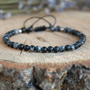 Peut inclure: Bracelet en pierres précieuses tachetées de noir et blanc avec une fermeture en cordon noir.