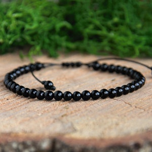 May include: A black onyx beaded bracelet with a black cord and adjustable closure. The bracelet is on a wooden surface.