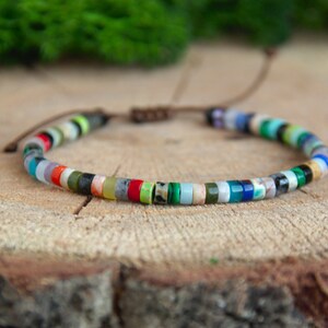 Puede incluir: Un brazalete de cuentas de colores con cierre de cordón marrón. El brazalete presenta una variedad de cuentas pequeñas y redondas en tonos de azul, verde, rojo, naranja y blanco.