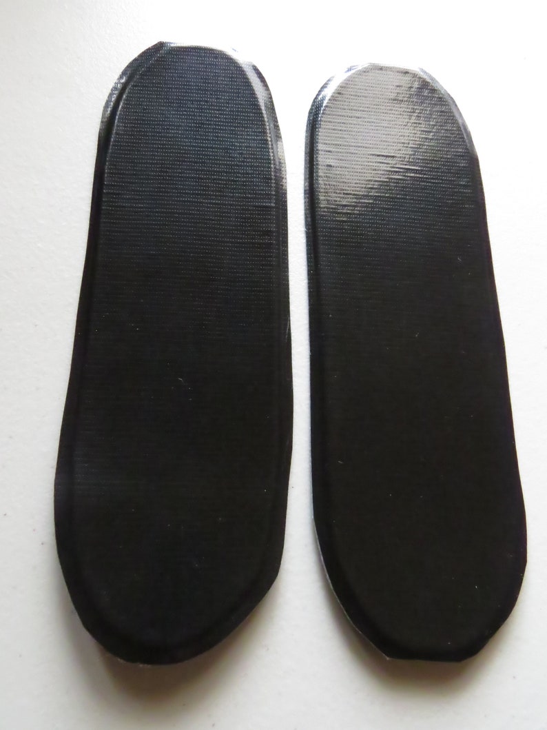Puede incluir: Dos plantillas de zapatos ovaladas de color negro.