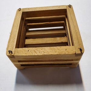 May include: A small, wooden hanging planter with four sides and a rectangular shape. The planter has a natural wood finish and four metal hooks for hanging.
