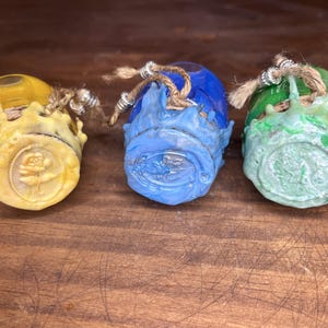 May include: Three small glass jars with wax seals. The jars are decorated with a yellow, blue, and green wax. Each jar has a different design on the wax seal.