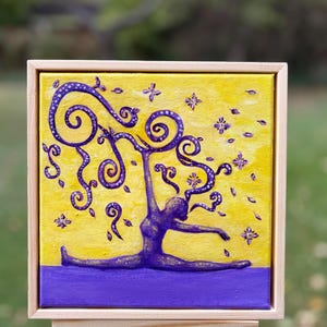 May include: A square canvas painting in a light wood frame depicts a purple figure performing a split against a bright yellow background. The figure has long, swirling purple hair with white dots, and small purple flower shapes float around.