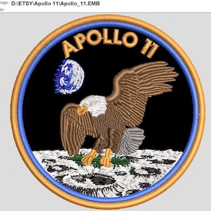 May include: A circular embroidered patch with a blue, gold, and white border. The center of the patch features a bald eagle landing on the moon with the Earth in the background. The text "APOLLO 11" is written in a white, bold font above the eagle.