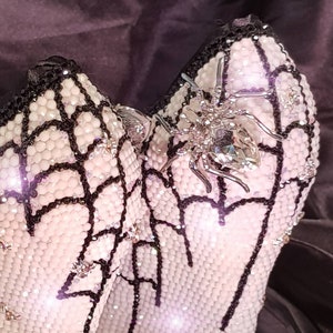 May include: A pair of white high-heeled shoes with black spiderweb designs and a sparkling silver spider embellishment.