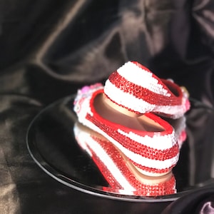 Puede incluir: Un par de zapatos planos de rayas rojas y blancas cubiertos de pedrería. Los zapatos se reflejan en un espejo plateado.