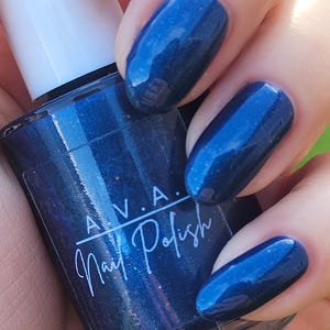 Peut inclure: Gros plan sur un flacon de vernis à ongles AVA et des ongles vernis. Le vernis à ongles est d'un bleu profond et chatoyant. Les ongles sont de forme ovale et ont une finition brillante. Le flacon a un bouchon blanc et une étiquette avec le texte "AVA Nail Polish".