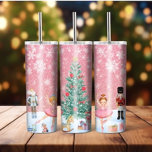 May include: Three pink glitter tumblers with a Christmas theme. Each tumbler features a different design: a ballerina, a Christmas tree, and a nutcracker. The tumblers have stainless steel straws.
