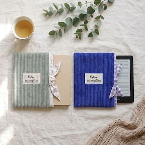 Puede incluir: Dos fundas rectangulares para libros de pana, una verde salvia y otra azul real, cada una con una etiqueta de tela blanca con el texto negro 'Votre inscription' y una cinta lateral. La funda verde tiene una cinta floral, la azul una de cuadros.