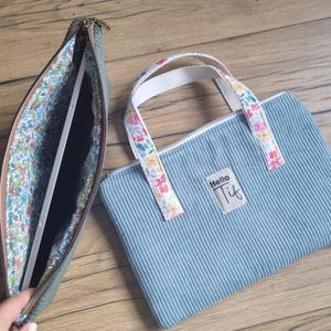 Può includere: Due borse di velluto a coste, una aperta, che mostra un tablet. La borsa aperta è verde oliva con interno floreale. L'altra è azzurra con manici floreali e la scritta "Hello Tif".