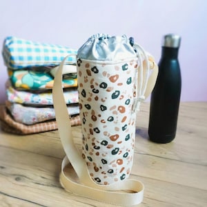 Puede incluir: Una taza de cerámica blanca con un asa negra y el texto "But First, Coffee" en negrita negra. La taza se encuentra sobre un fondo neutro, resaltando su diseño sencillo.