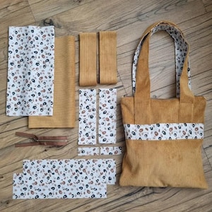 Può includere: Un set di pezzi di tessuto per un progetto di borsa tote. I pezzi sono in velluto a coste color senape e in tessuto bianco con stampa leopardata marrone e nera. La borsa è già assemblata ed è realizzata in velluto a coste color senape con rifinitura in stampa leopardata marrone e nera.