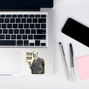 Puede incluir: Una pegatina en blanco y negro de Sigmund Freud con un cigarrillo en la mano y el texto "YOUR MUM" encima. La pegatina est&aacute; en un port&aacute;til plateado.