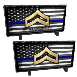 May include: A black and white American flag with a blue stripe and a gold chevron rank insignia. The flag is on a slate plaque with a black stand. The text "OFFICER NAME AND RANK Department Name" is printed below the flag.