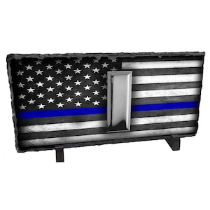 May include: A black and white American flag with a blue line and a silver badge on a slate plaque with black metal stand.