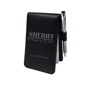 May include: Black leather notebook with a pen holder and the words "SHERIFF To Protect and To Serve" engraved on the front. The notebook also has the text "Your Text Here" engraved on the front.