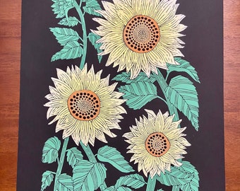 May include: A black and white print of three sunflowers with green leaves and stems. The print is numbered 5/20 and signed "B. Calon '22".