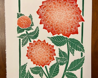 May include: A green framed print of a red and orange dahlia flower with green leaves. The print is numbered 6/20 and signed "Dahlias" and "B. Carlson 21".