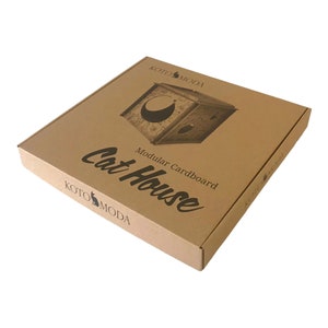 Pode incluir: Uma caixa de cart&atilde;o castanho com o texto "Modular Cardboard Cat House" e o logotipo "KOTO MODA" impresso nela. A caixa apresenta um gr&aacute;fico de uma casa para gatos com uma lua e estrelas.