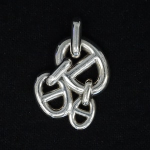 May include: A silver-toned pendant with a nautical anchor chain link design. The pendant features multiple interlocking links, creating a three-dimensional effect. The background is a solid black.