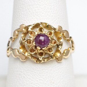 May include: A gold ring with a purple gemstone set in a delicate, ornate design.