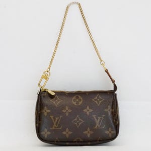 May include: Brown monogrammed handbag with a gold chain strap. The small bag features a zipper closure and a gold clasp. The bag is a classic design with a repeating pattern of the brand's logo.