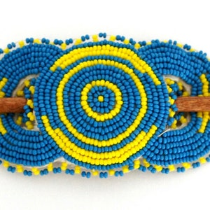 May include: A beaded hair stick with three circular designs. The designs are made of blue and yellow beads and are arranged in a concentric circle pattern. The stick is made of wood.