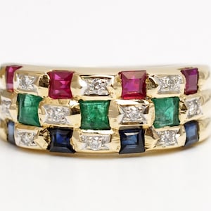 May include: A gold band ring with a multi-colored gemstone design. The ring features emerald, ruby, sapphire, and diamond stones set in a geometric pattern.