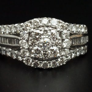 May include: A silver ring with a large, round, center diamond surrounded by smaller diamonds. The ring has a band with smaller diamonds set in a channel setting.