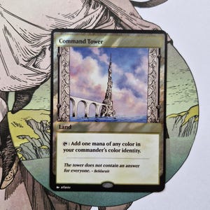 May include: A Magic: The Gathering trading card titled Command Tower, featuring a tall stone spire rising from the water connected by an arched bridge under a cloudy sky. The card text reads: Add one mana of any color in your commander's color identity.
