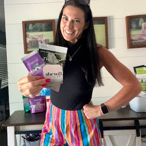 May include: A woman holding various Thrive products, including a purple and white packet, a pink and white packet, and a white packet with the text "she will thrive on".