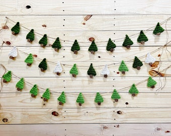 Könnte beinhalten: Eine festliche Girlande aus gehäkelten Weihnachtsbäumen in verschiedenen Grün- und Weißtönen, jeder mit einem braunen Stamm. Die Bäume sind auf Schnur aufgereiht und in Reihen vor einem Holzgrund angeordnet, was eine charmante Weihnachtsdekoration ergibt.