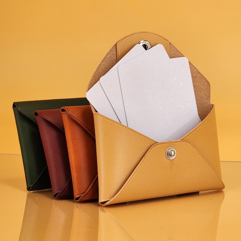 May include: Four leather wallets in different colors, including green, brown, orange, and yellow. The yellow wallet is open and has a white card inside.