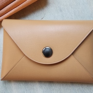 May include: A tan leather envelope-style wallet with a black button closure.