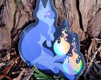 May include: A die-cut sticker featuring a stylized blue cat with pink eyes sitting next to two iridescent, holographic flames. The sticker has a black border and includes the text CURIOUSNATURE.ART printed along the left side of the cat's body.