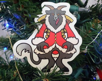 May include: A die-cut sticker featuring a cartoon Krampus character with dark gray fur, horns, and a long tongue. The figure wears a red coat with white fur trim and gold bells, carrying a bundle of sticks on its back against a white background.