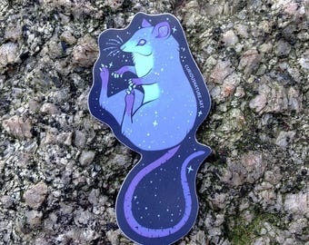 May include: A die-cut sticker featuring a stylized opossum with a celestial theme. The opossum is colored in shades of blue and purple with white star patterns. The text CURIOUSNATURE.ART is printed along the right side of the sticker.