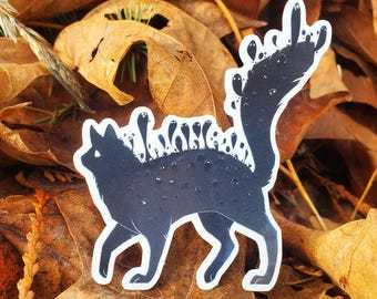 May include: A dark blue sticker featuring a stylized cat with a unique design. The cat has a white outline and is covered in small, white, bubble-like shapes. The cat's tail extends upwards, also adorned with white shapes. The sticker is set against a backdrop of autumn leaves.