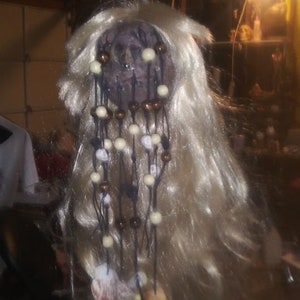 May include: A doll's head with long blonde hair, decorated with brown and white beads and seashells.