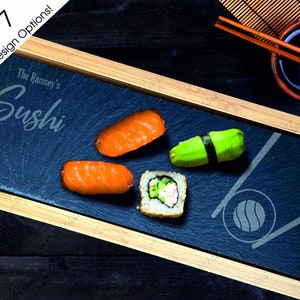 May include: A slate serving tray with a wooden frame, featuring the text "The Ramsey's Sushi" and a design of chopsticks and a sushi roll. The tray is filled with four pieces of sushi, including two salmon nigiri, one avocado maki, and one cucumber maki.