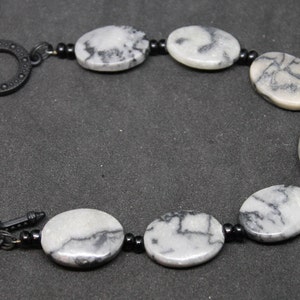 May include: A black and white marble bracelet with a black metal clasp. The bracelet is made of oval-shaped beads with black accents.