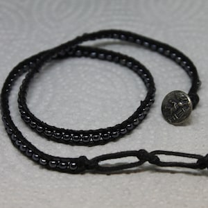 May include: A black leather wrap bracelet with black beads and a silver button closure.