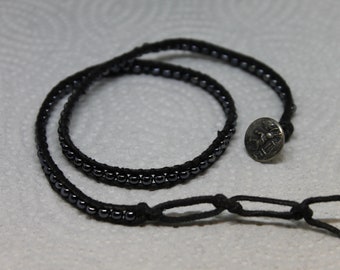 A hand made unisex wrap bracelet features hematite beads surrounded by black leather cording with a pewter button and two loops for closure.