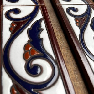 May include: Close-up of decorative ceramic tiles with a white background and a repeating pattern of blue, brown, and orange swirls.