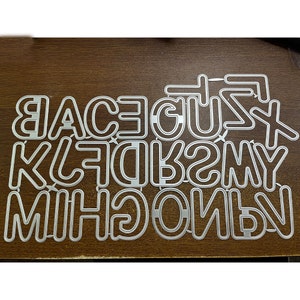 Puede incluir: Un conjunto de plantillas de letras del alfabeto de metal para manualidades. Las letras están en mayúsculas y están dispuestas en orden aleatorio.